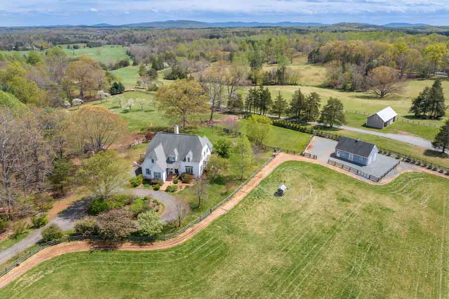 Aerial view of a charming white charlottesville country property with fenced pastures, a barn, and open fields in Charlottesville, Virginia countryside.