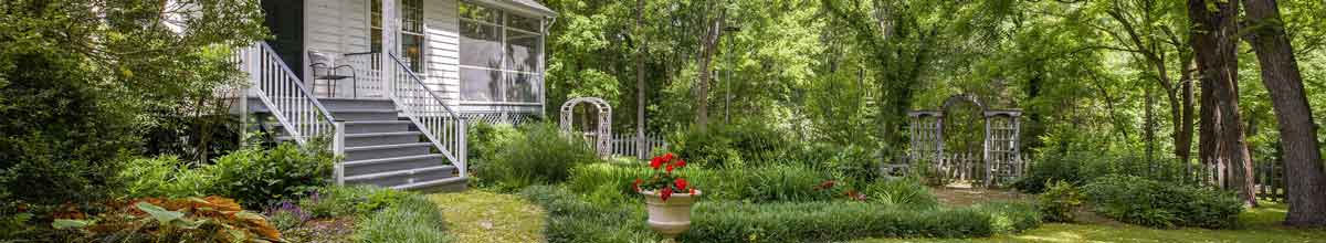 Charlottesville country property featuring a charming farmhouse with a wraparound porch, historic log cabin, outdoor living areas, and wooded landscape.